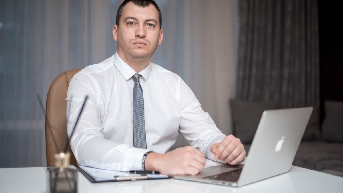 A confident businessman in corporate attire working diligently on a laptop in a modern office setting.